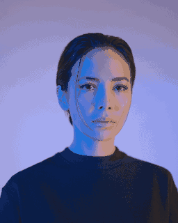 A close portrait is lit in blue against a pale purple background.