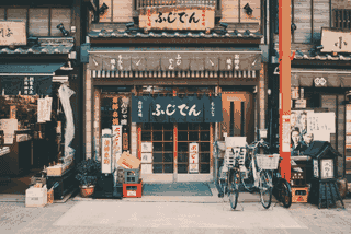 Bicycles are parked outside a small Japanese storefront with signs and windows.