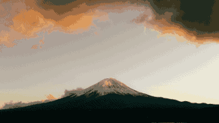 Mount Fuji stands beneath low clouds edged with warm light.