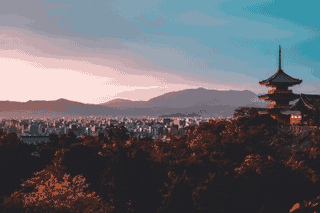 A pagoda overlooks a dense city under a warm evening sky.