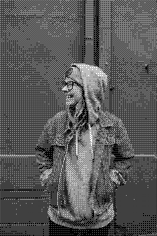 A person wearing glasses, a hood, and a denim jacket stands against a blue wall. Dithered grayscale treatment.