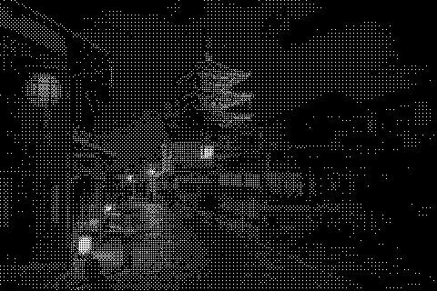 A narrow street leads toward a pagoda at night, with lit buildings along the way. Dithered grayscale treatment.